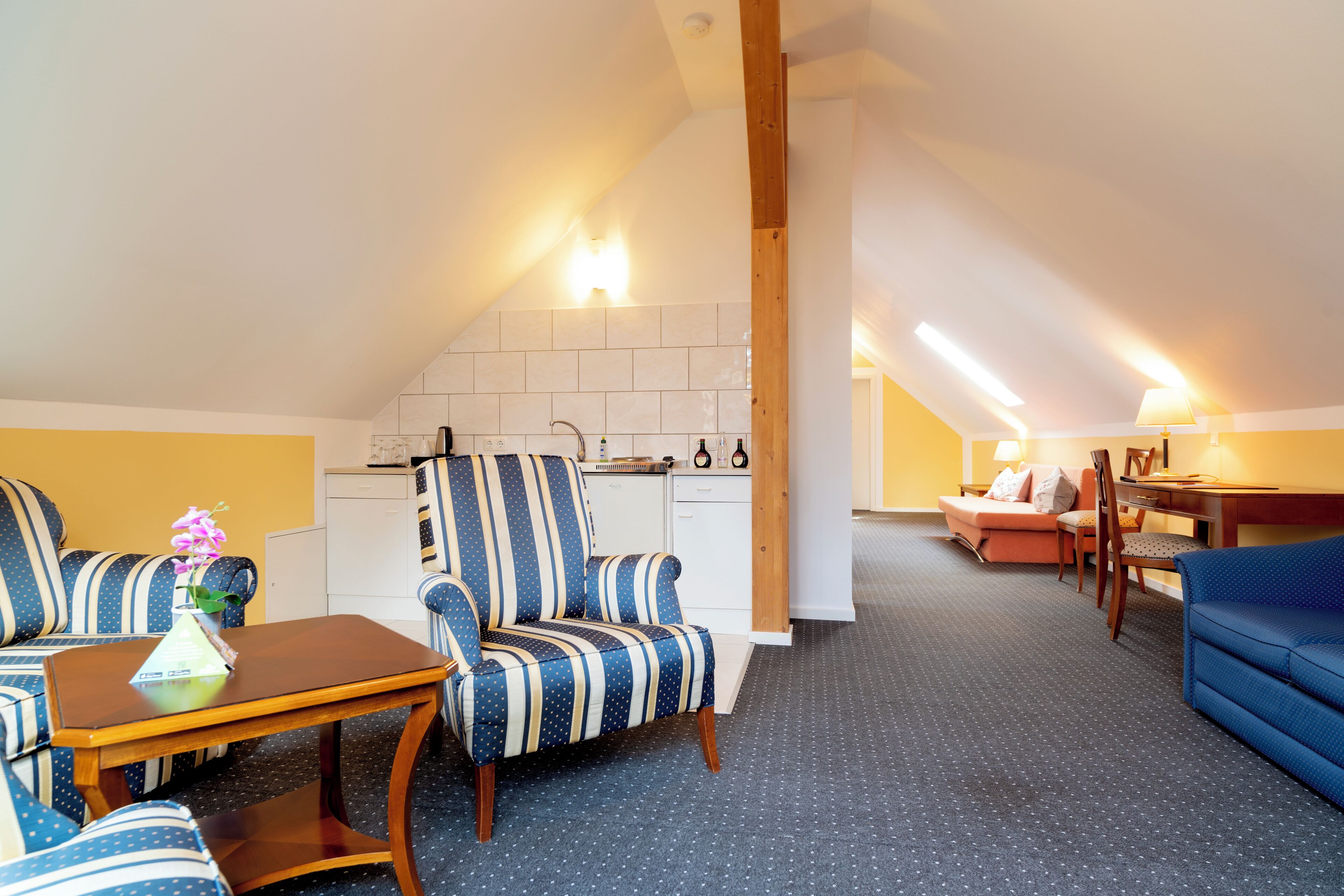 Una habitación acogedora con un sillón a rayas, una mesita, un sofá y una zona de cocina con lavavajillas.
