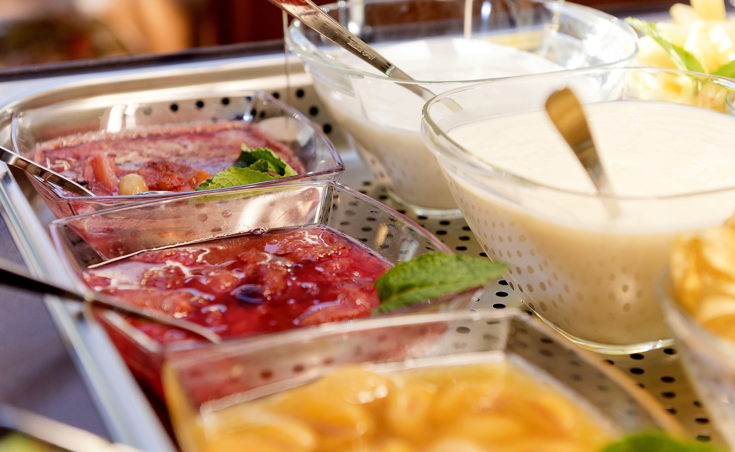 Buffet amb diverses opcions gastronòmiques, incloent fruites, iogurt i altres plats.
