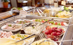 Un bufé con diversas opciones de comida, incluyendo carnes, ensaladas y un recipiente de ensalada que indica que es queso crema granulado.