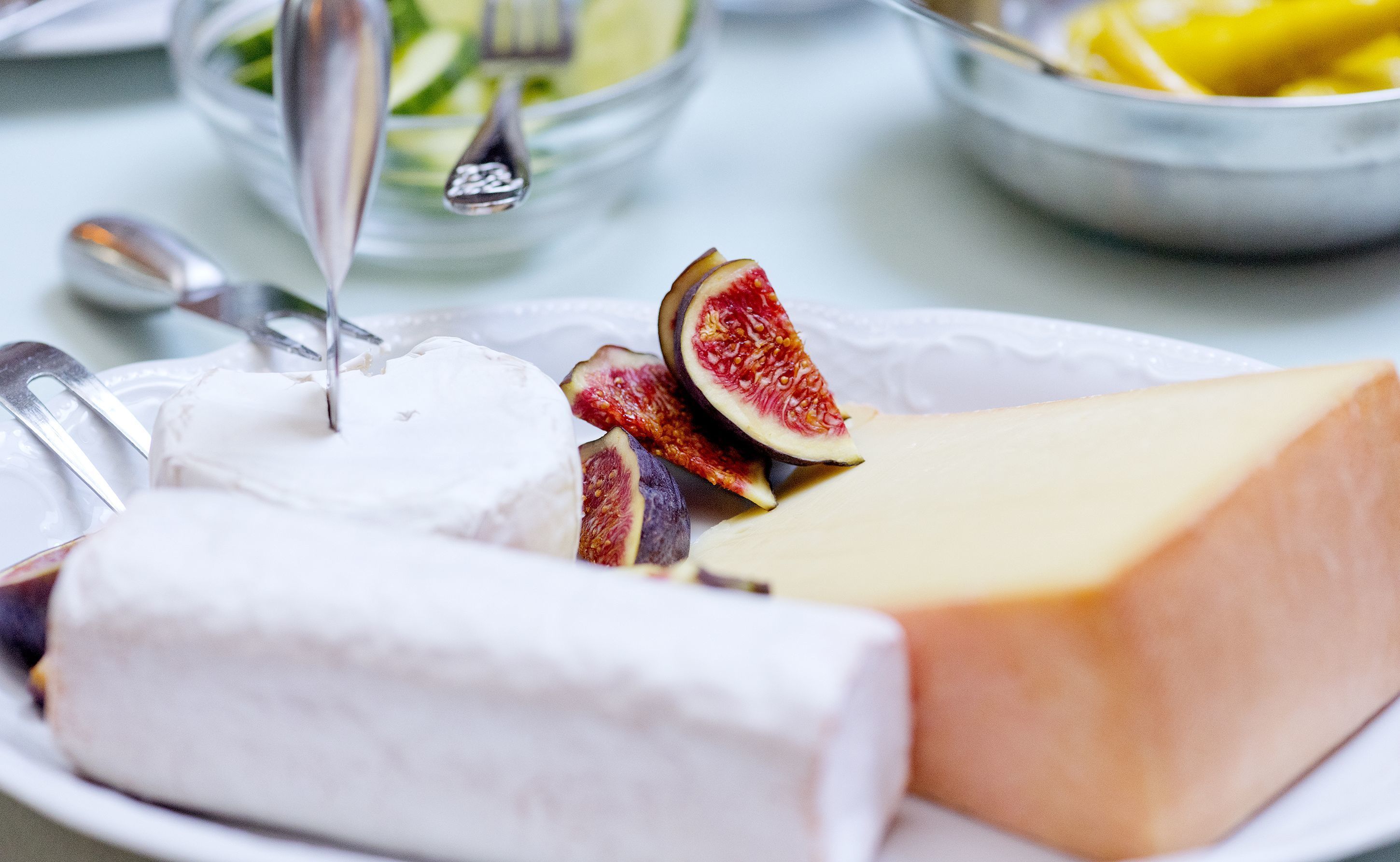 A plate with a large piece of cheese, a wedge of white cheese, and sliced figs.