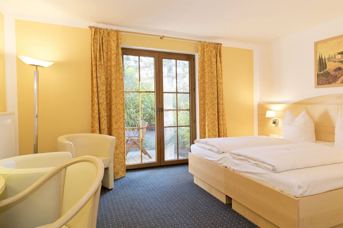 Een hotelkamer met een bed, een stoel, een lamp, een schilderij en een raam met gordijnen.