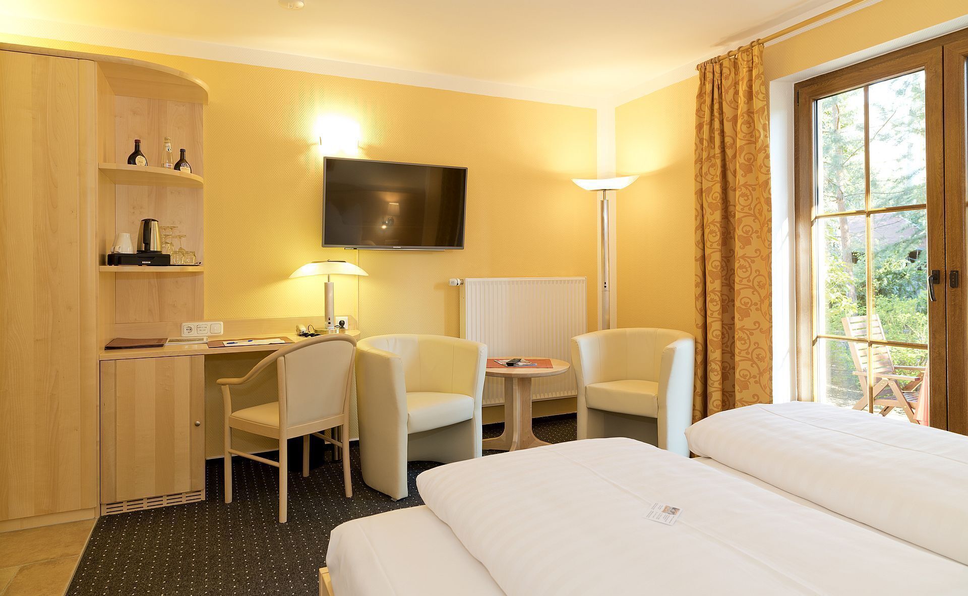 Een hotelkamer met een bed, twee stoelen, een bureau met lamp, een televisie en een raam met gordijnen.