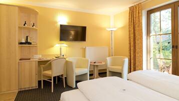 Een hotelkamer met een bed, twee stoelen, een bureau met lamp, een televisie en een raam met gordijnen.