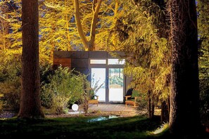 Un bâtiment moderne à la façade en verre, entouré d’arbres et d’un petit étang.