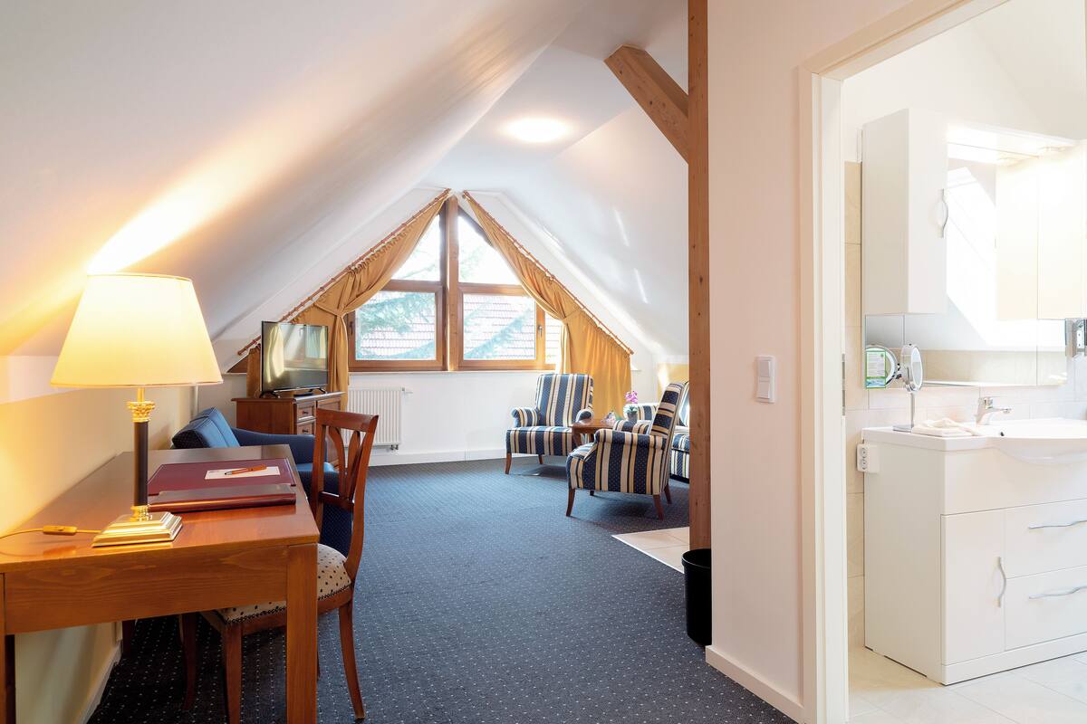Een kamer met een eettafel, stoelen, een lamp, een bank, een televisie en een raam met gordijnen.
