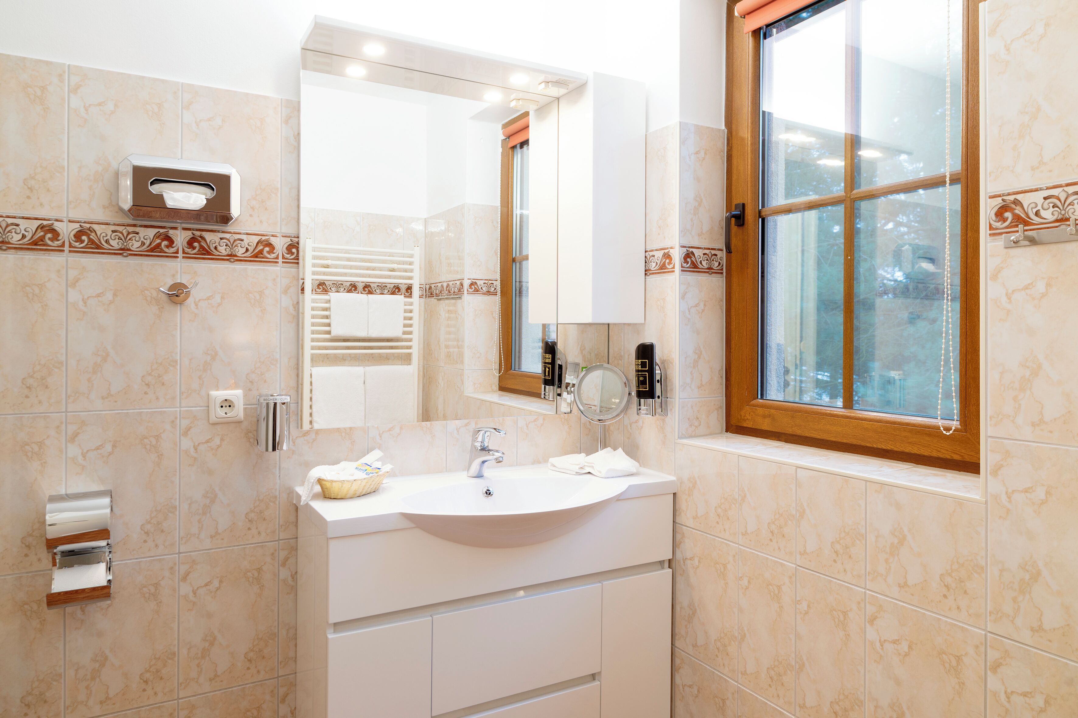 Un baño con lavamanos, espejo, toallero y ventana.