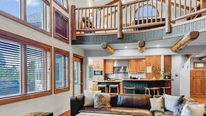 A spacious living area with a high ceiling, a wooden staircase, and a kitchen with wooden cabinets. - Above the Fray (Breckenridge)