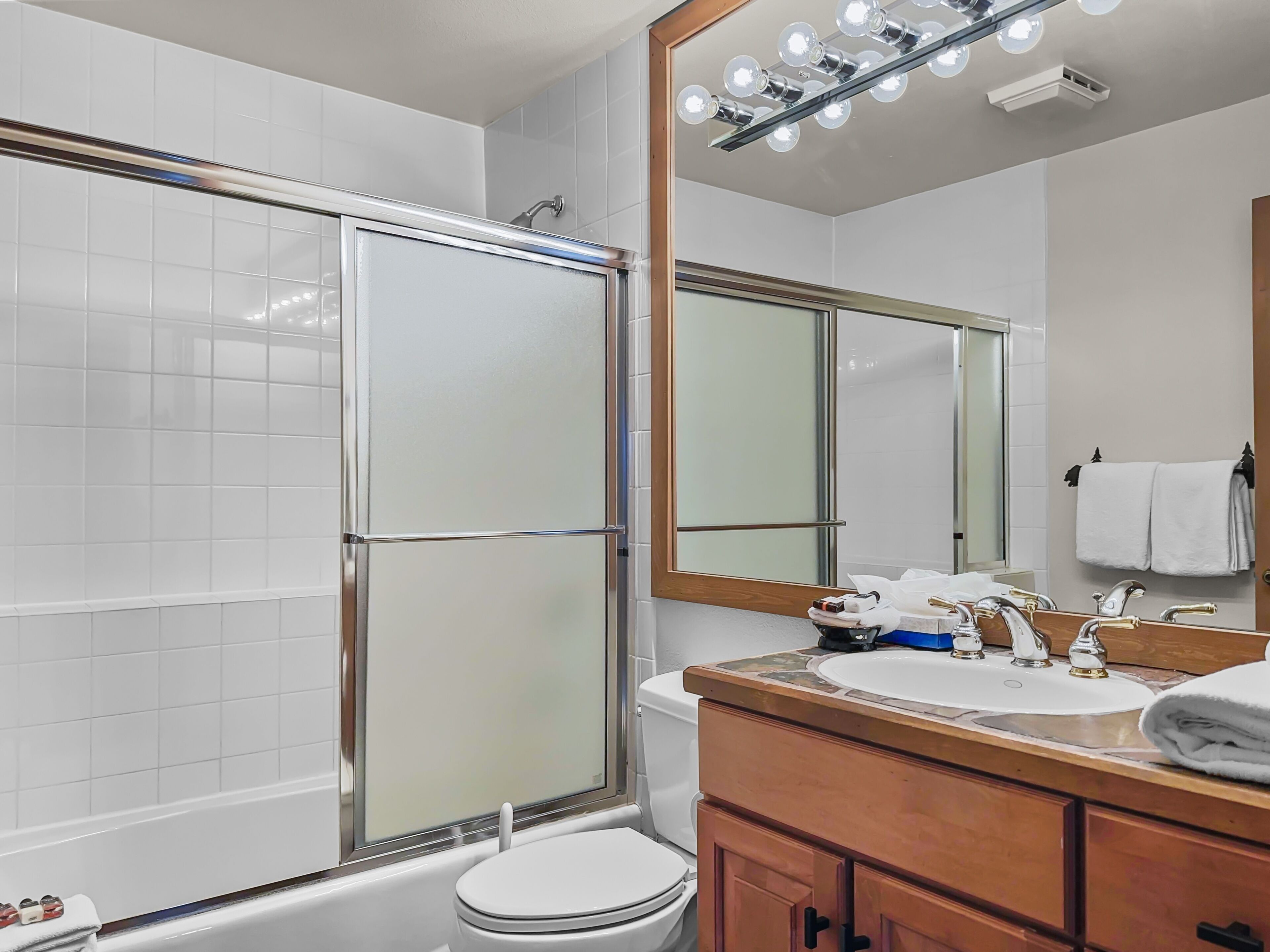 A modern bathroom with a glass shower enclosure, a white toilet, a sink with a wooden vanity, and a mirror with lights above.