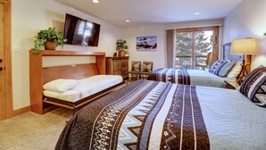 Un dormitorio con dos camas, televisión y ventana con vista a árboles.
