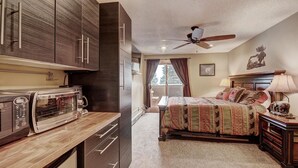 A compact hotel room with a kitchenette, a bed with a patterned bedspread, a ceiling fan, and a window with curtains. - CM417H Copper Mtn Inn Studio Bedroom 1Bathroom Hotel Room (Copper Mountain)
