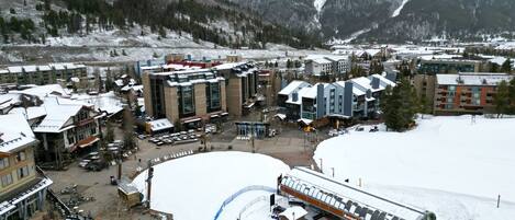 A snow-covered resort with multiple buildings, a ski lift, and a mountainous backdrop.