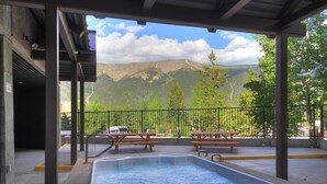 Espaço ao ar livre coberto com piscina, mesas de piquenique e vista para as montanhas.