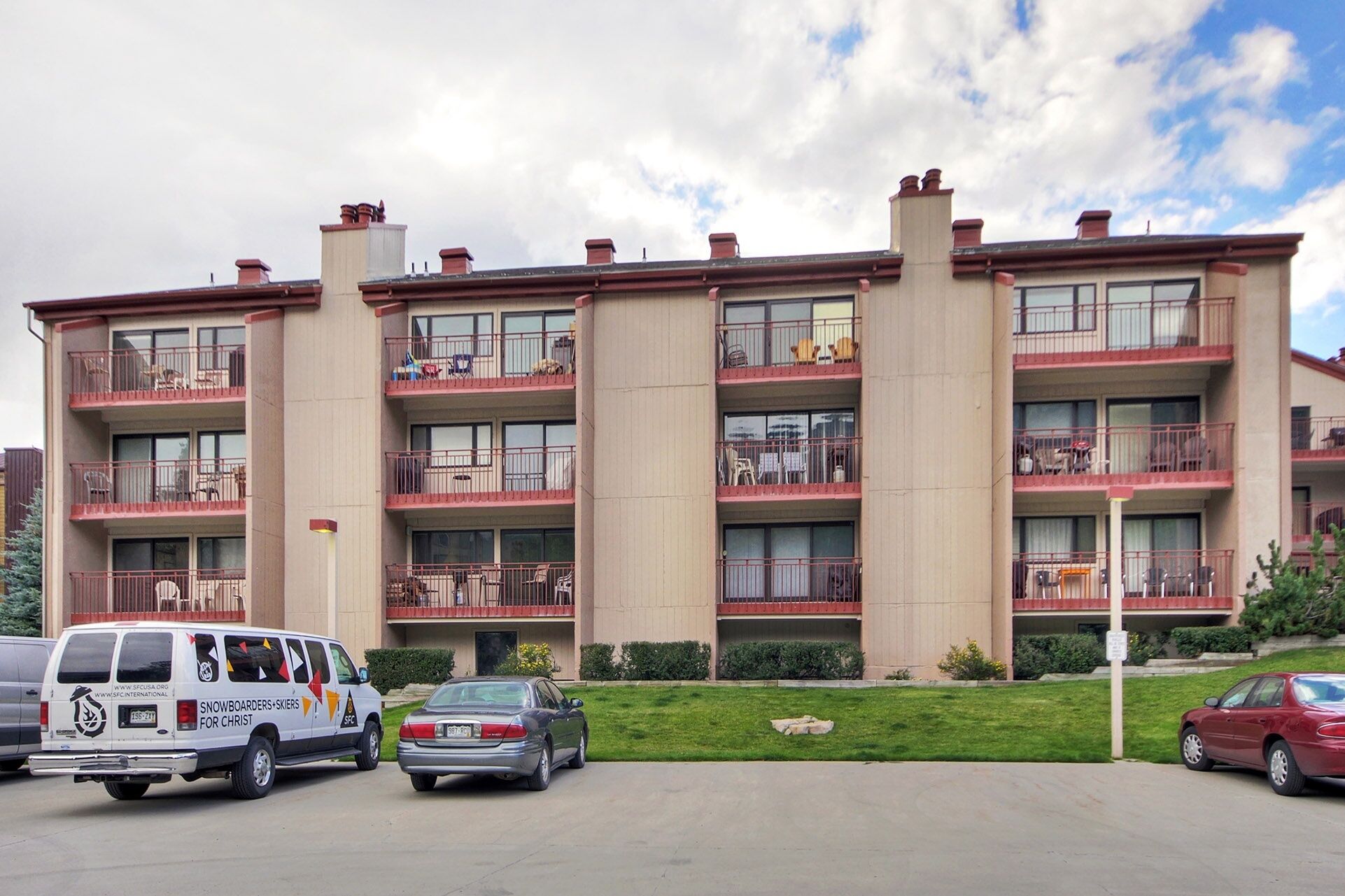Un immeuble à plusieurs étages doté de balcons, d’un parking et d’un espace vert.