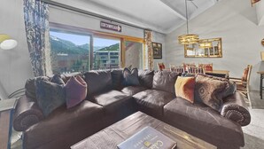 A living room with a large L-shaped sofa, a dining table with chairs, and a view of mountains through large windows. - Peregrine Lodge-Remodeled Kitchen-Steps to Super Bee Lift - PG309 by RedAwning (Copper Mountain)