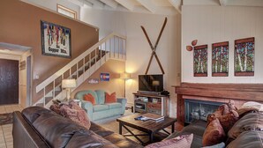 A cozy living room with a fireplace, a television, and a staircase. - Peregrine Lodge-Remodeled Kitchen-Steps to Super Bee Lift - PG309 by RedAwning (Copper Mountain)