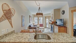 A kitchen with granite countertops, a stainless steel sink, wooden cabinets, a hanging light fixture, and a dining area with a table and chairs. - Taylors Crossing In The Heart Of Copper Center Village - Short Walk to American Eagle/American Flyer - TX312 by RedAwning (Copper Mountain)