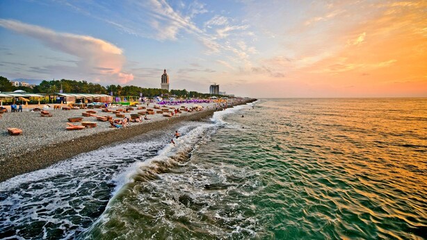 Una playa con una fila de sillas y sombrillas, una torre al fondo y el océano.
