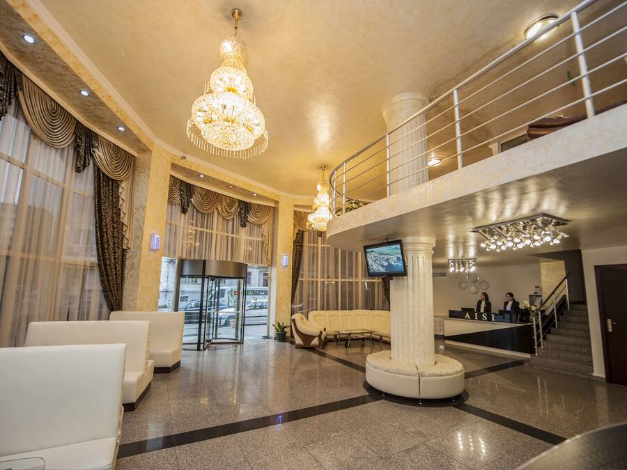Un hall espacioso con una imponente lámpara de araña, una mesa de recepción, un sofá blanco curvo y una escalera que conduce a un nivel superior.