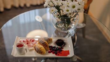 A glass table with a white plate of pastries, a small vase with white flowers, and a glass of red liquid.