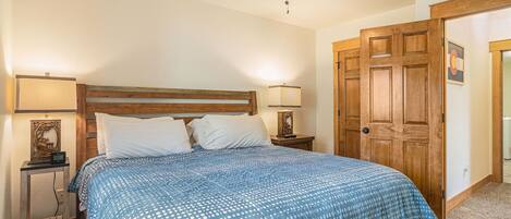 A bedroom with a wooden headboard, a bed with a blue polka dot bedspread, two bedside lamps, a nightstand, and a wooden door.