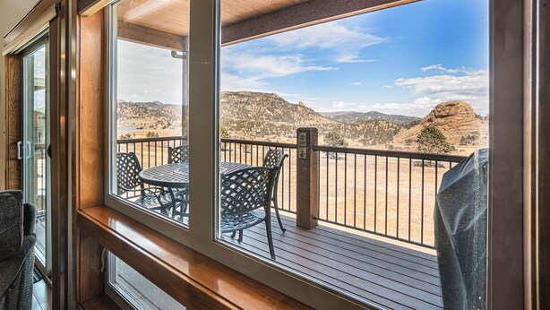 A balcony with a table and chairs, overlooking a mountainous landscape.