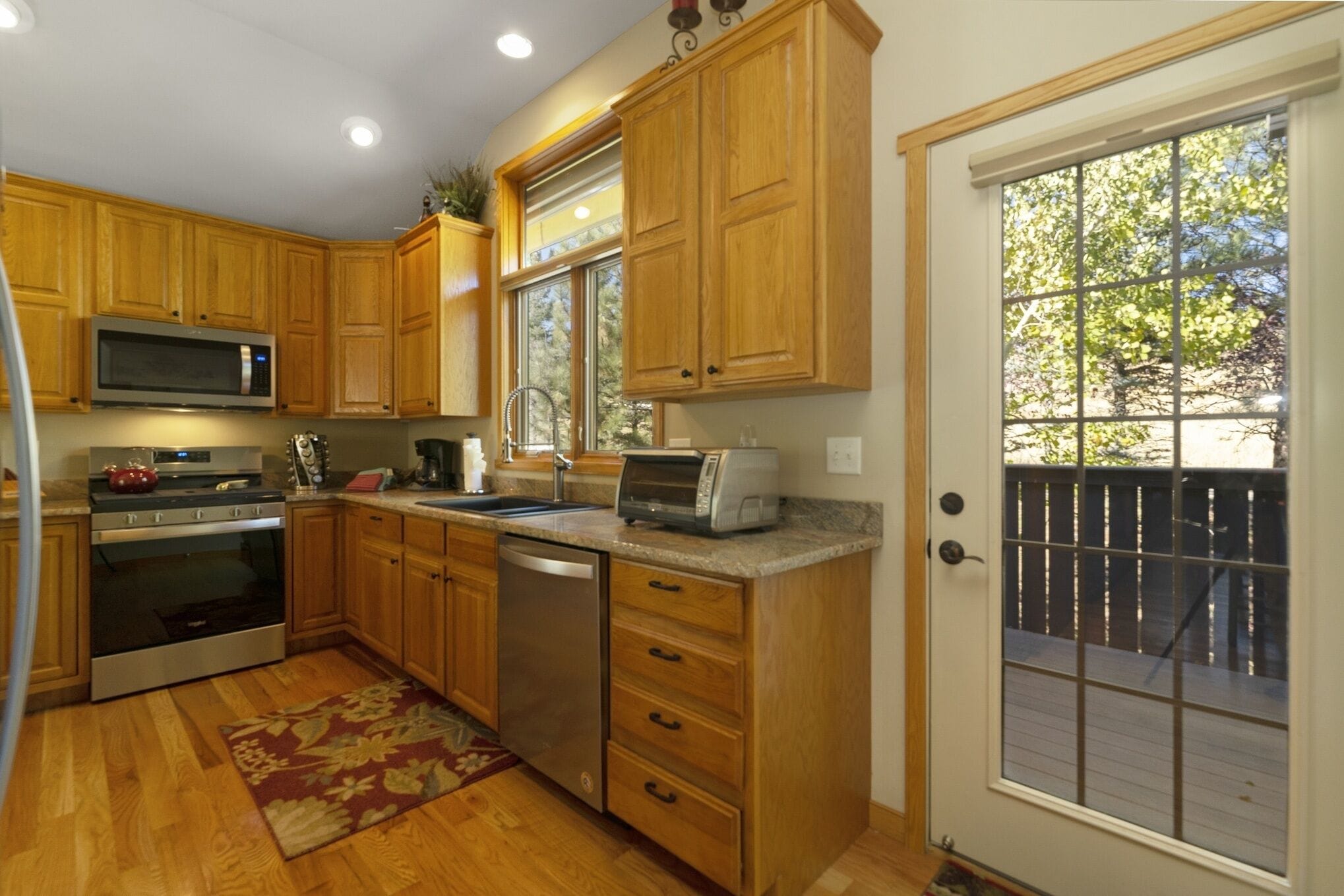 A kitchen with wooden cabinets, stainless steel appliances, and a large window with a view of a backyard.
