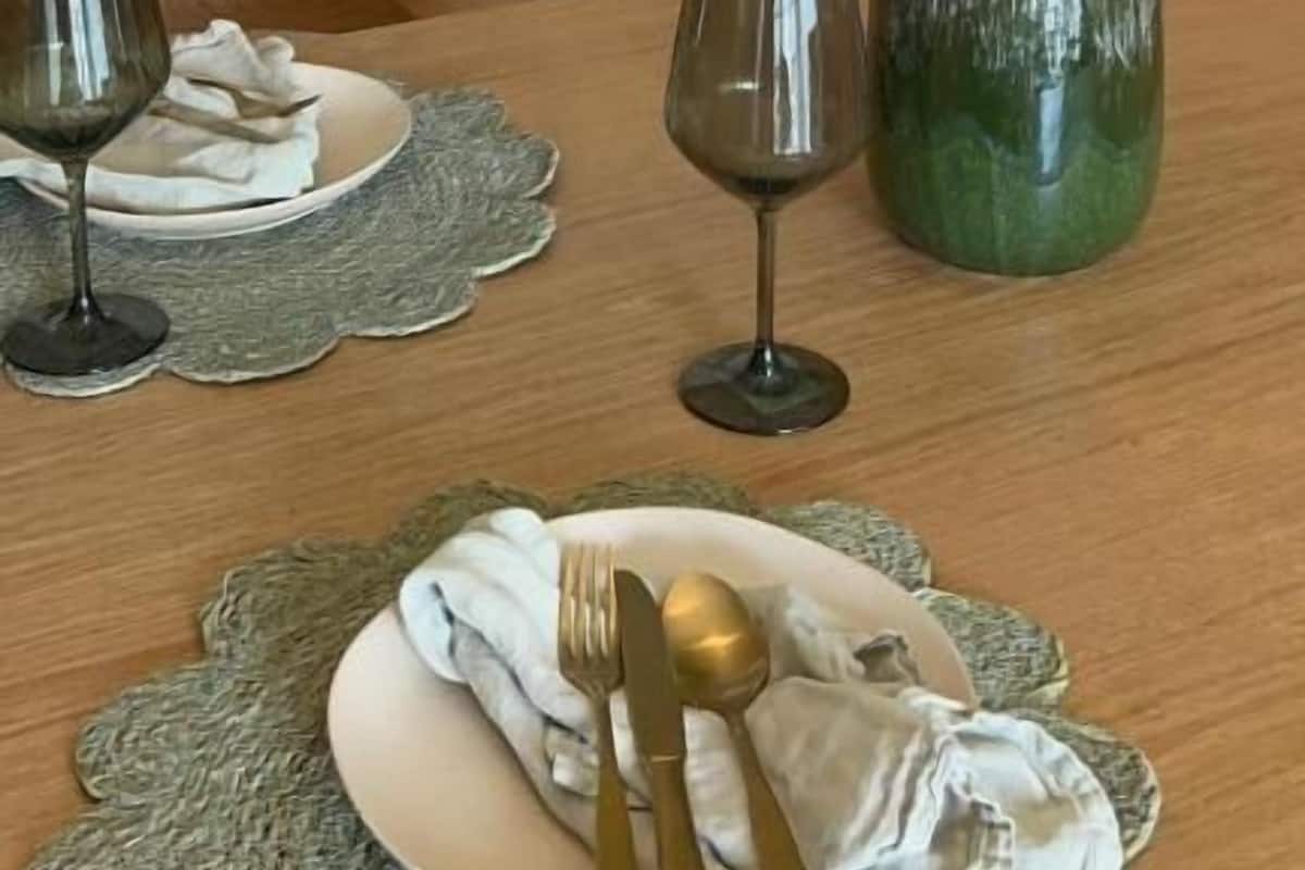 A dining table with a vase of green leaves, two wine glasses, and cutlery on a placemat.