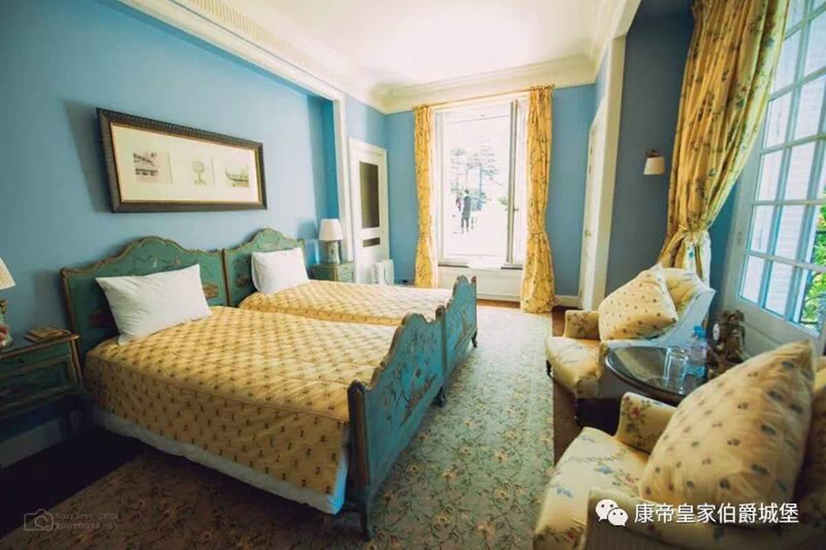 A room with two beds, a chair, a table, and a window with curtains.
