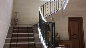 Un magnifique escalier, orné de rampes noires travaillées et de marches recouvertes d’une moquette à motifs, mène à un palier doté d’une grande fenêtre et d’un vase décoratif.