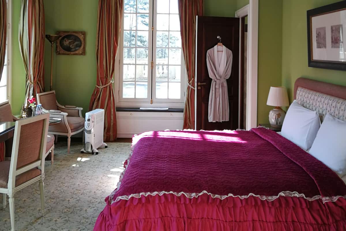 A bedroom with a large bed, a chair, a desk, and a window with curtains.