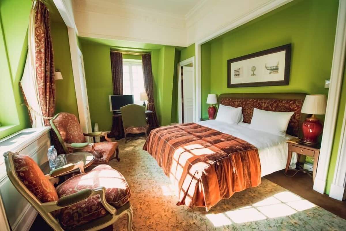A hotel room with a large bed, a sitting area with a chair and a small table, a television, and a window with curtains.