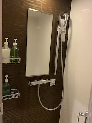 Un baño con espejo, cabezal de ducha de mano y dispensadores de jabón en un estante.