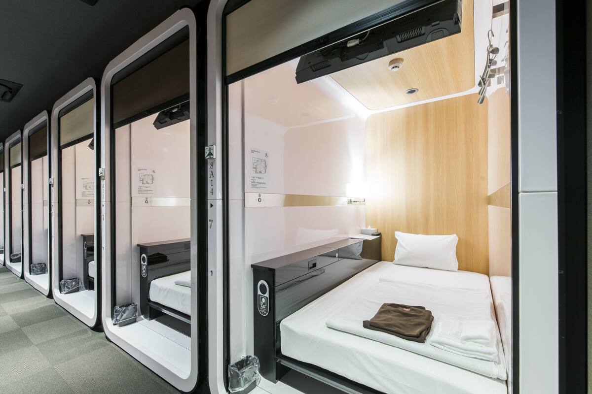 A row of single beds in a train car with wooden paneling and a small table with a lamp.