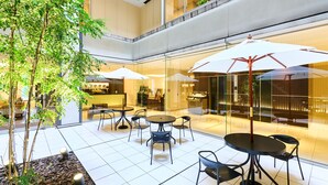 A modern indoor patio area with glass walls, tables, chairs, and umbrellas.