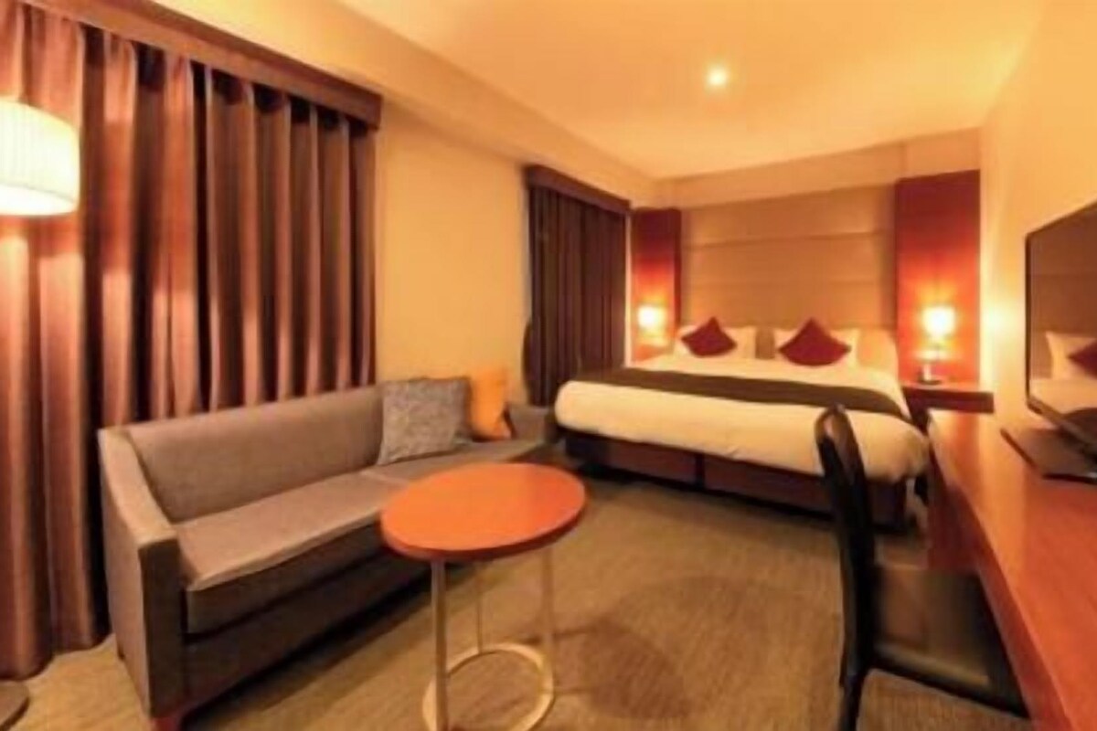 A hotel room with a bed, a sofa, a TV, and a small table.