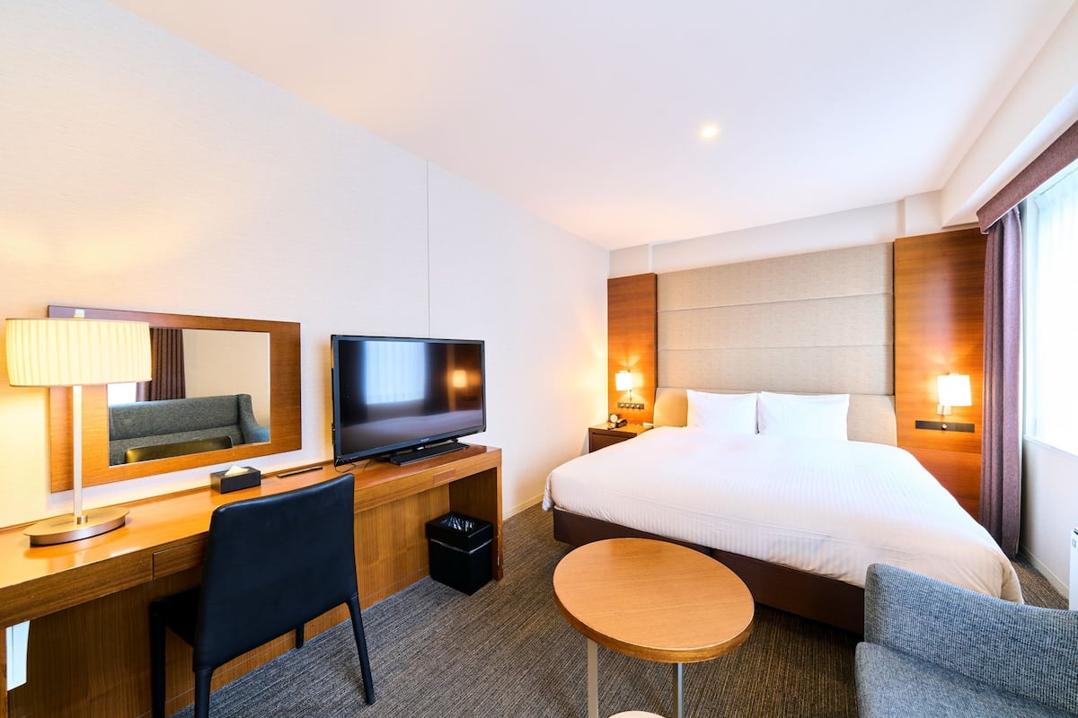 A hotel room with a bed, TV, desk, chair, and bedside table.