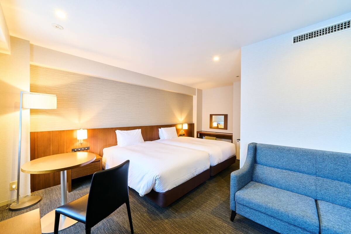 A hotel room with a large bed, a desk, a chair, a sofa, and a lamp.