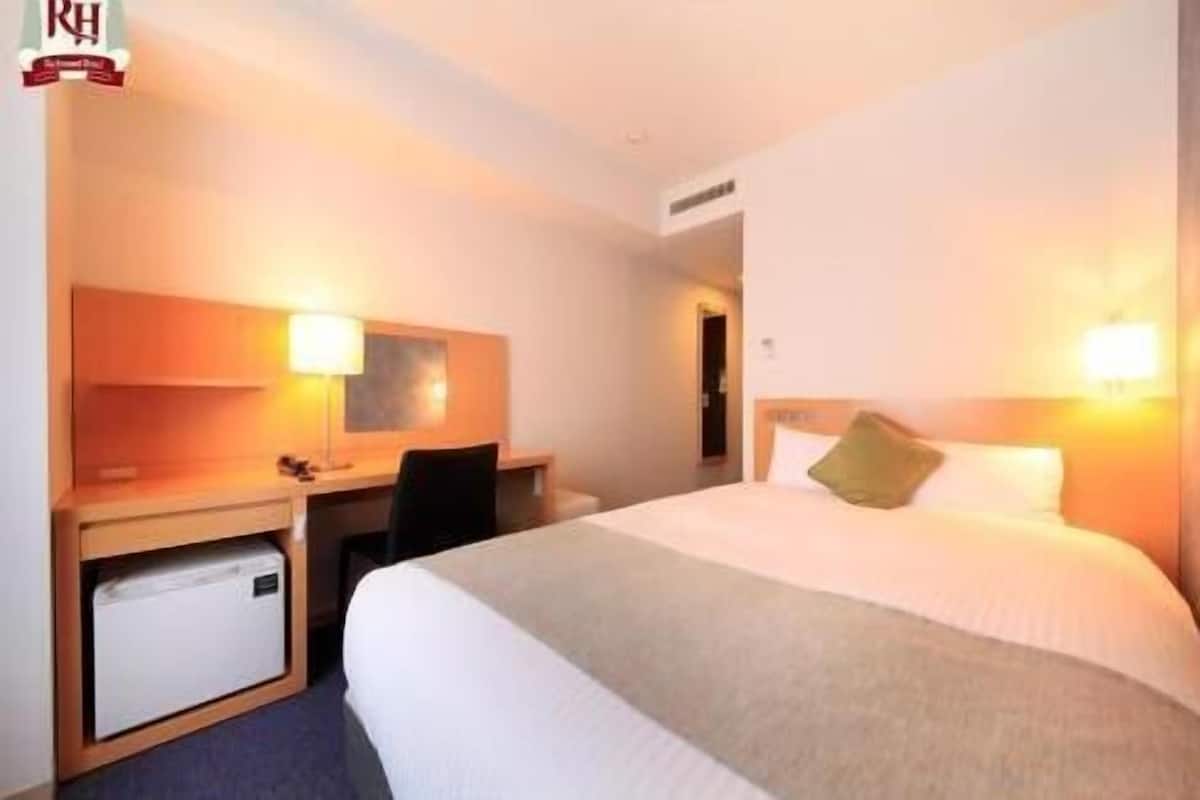 A hotel room with a bed, desk, chair, and a small cabinet.