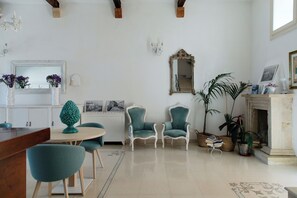Een woonkamer met een open haard, twee turquoise fauteuils, een ronde tafel en een spiegel aan de muur.