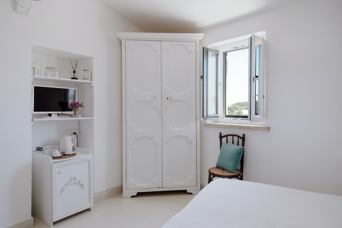 A bedroom with a bed, a wardrobe, a chair, and a window with a view.