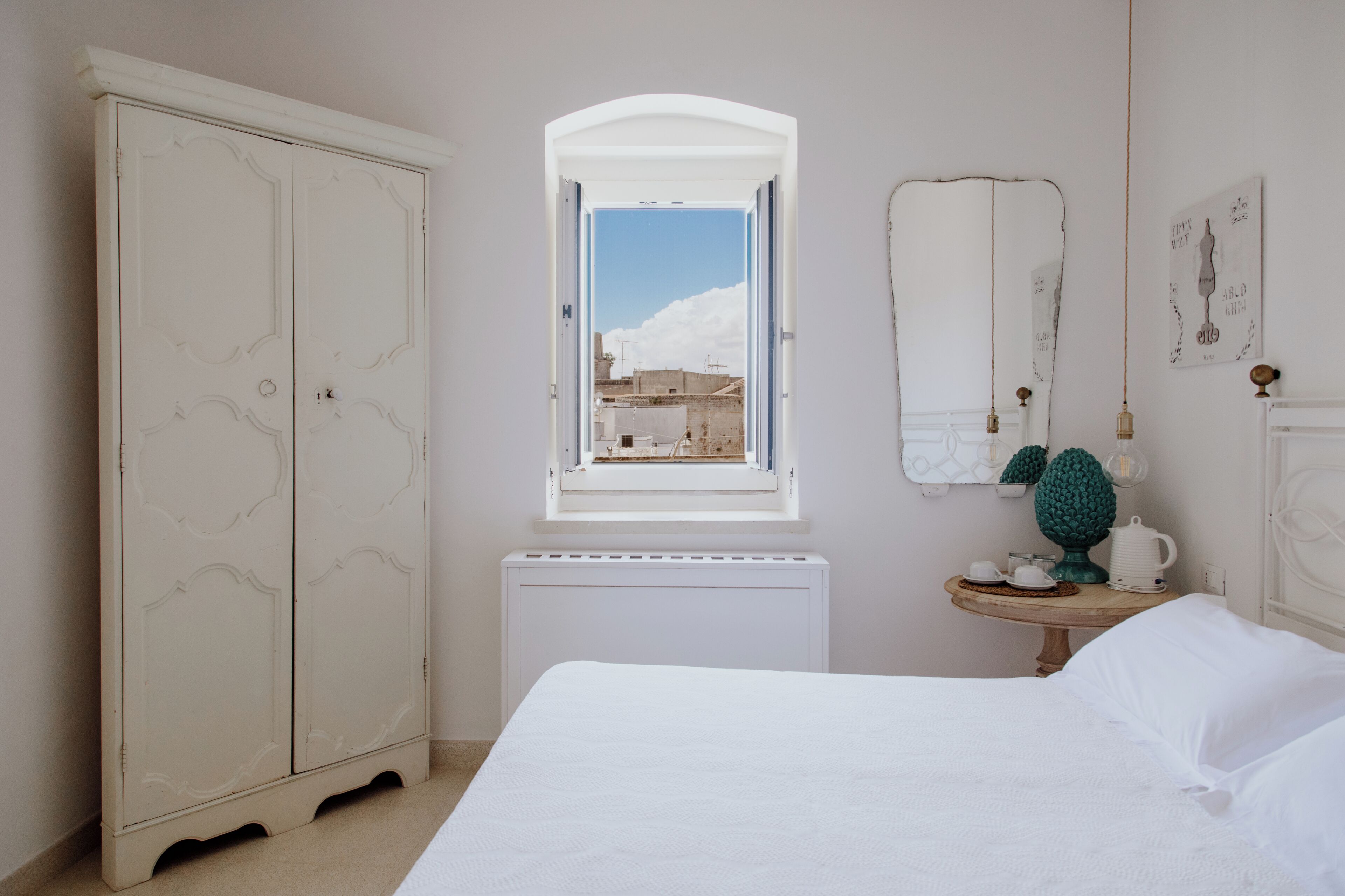 Un dormitorio con un armario grande, una mesita de noche con lámpara y una ventana con vistas a edificios.
