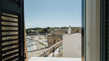 Vista desde una ventana sobre una zona costera con playa, un muro de contención marítimo y un edificio histórico de piedra.