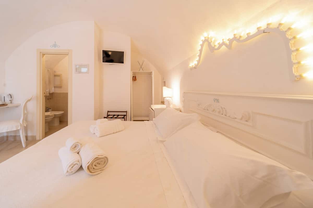 A hotel room with a large bed, a television, and a mirror with lights.