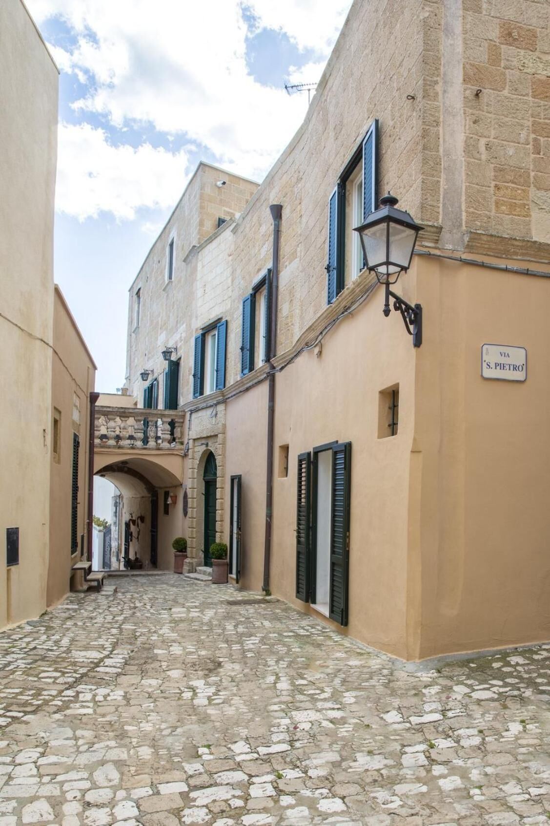 A narrow cobblestone street flanked by buildings with stone facades and shutters.