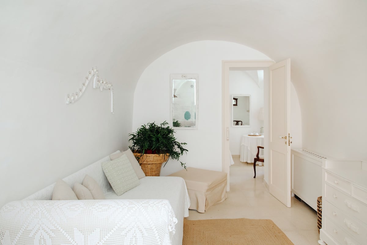 A minimalist bedroom with a bed, a bedside table, a plant, and a white wardrobe.