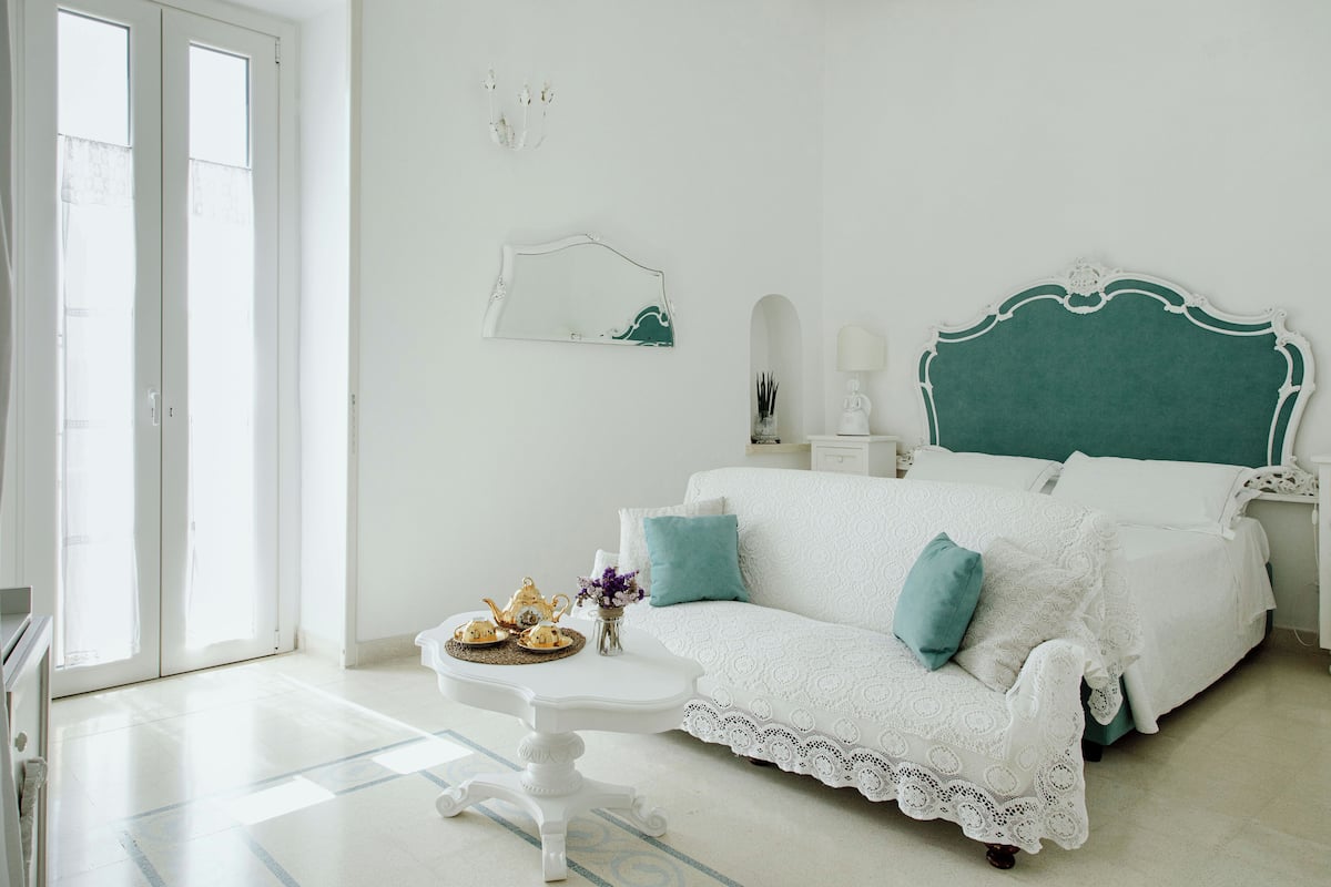 A bedroom with a white bed, teal pillows, a white dresser, and a white nightstand.