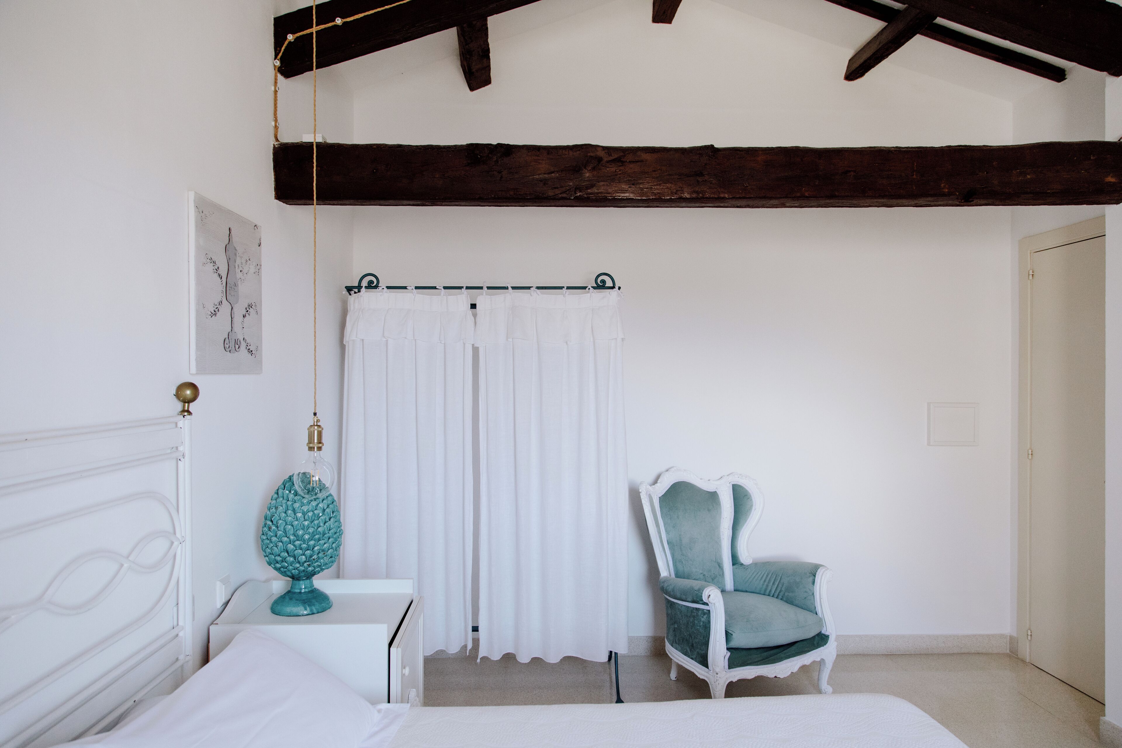 Un dormitorio con una cama blanca, una mesita de noche blanca, una lámpara verde aguamarina, una cortina blanca y una silla verde aguamarina.