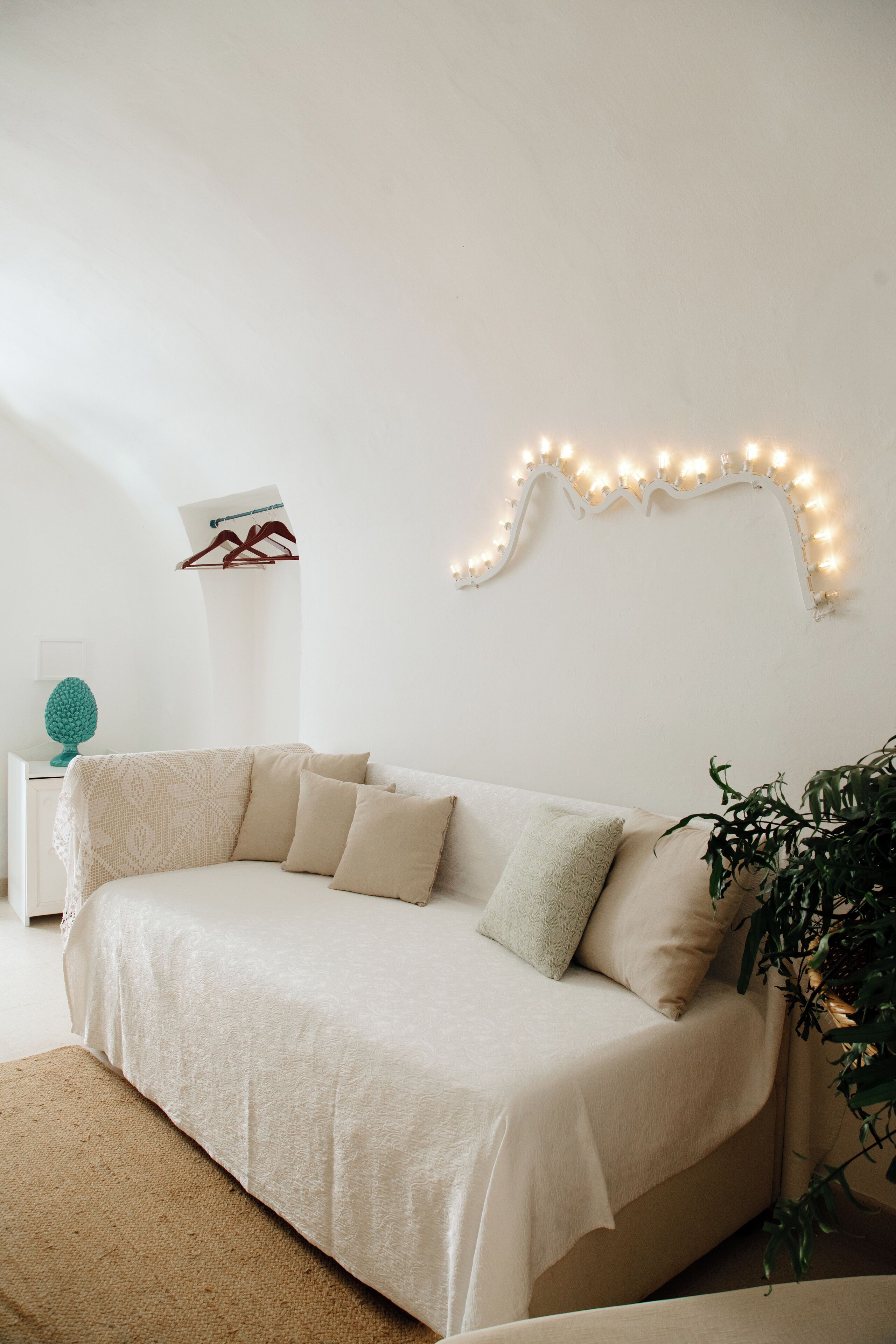 A cozy room with a beige sofa, a small white side table with a teal decorative object, and a wall-mounted light fixture.