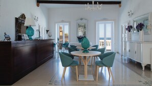 A spacious dining area with a round table and teal chairs, a dark wooden bar, and a chandelier.