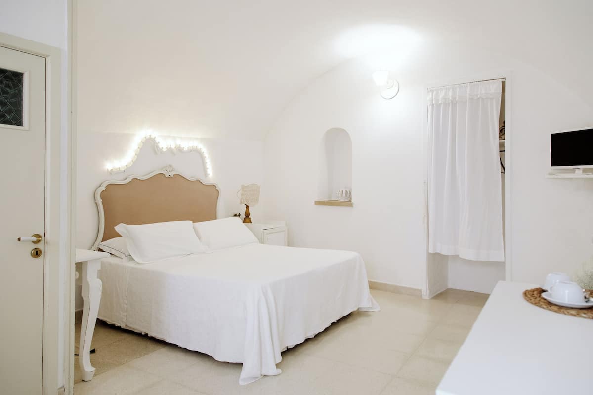 A bedroom with a bed, bedside table, lamp, and a TV mounted on the wall.